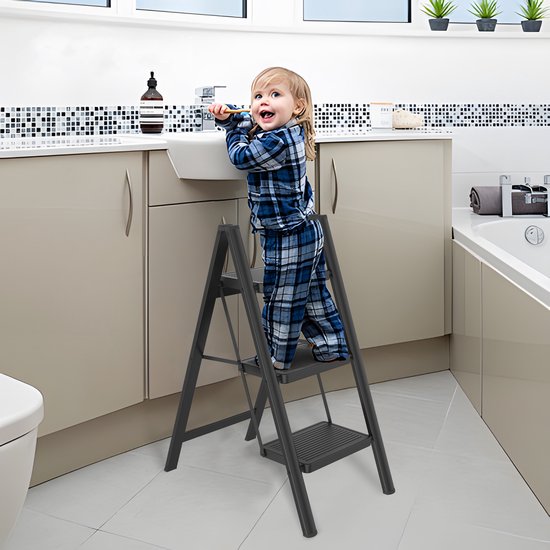 Een kind in pyjama staat op een zwarte 3-treden trap in een badkamer.