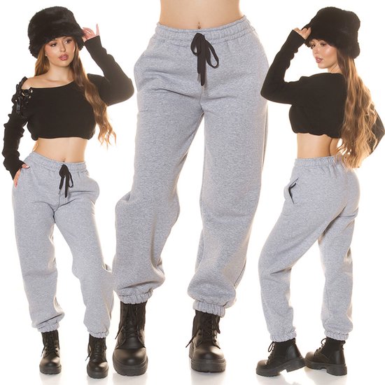 Grijze joggingbroek met trekkoord, gedragen door een model met zwarte crop top en zwarte hoed.
