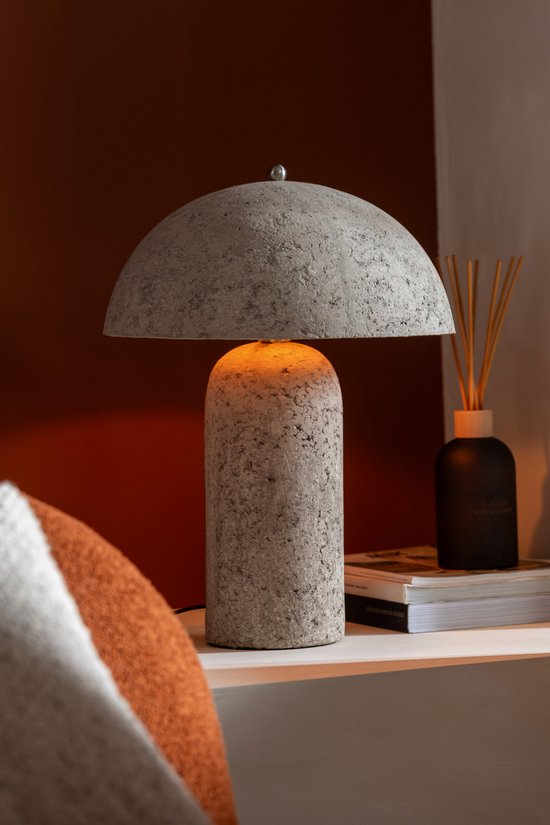 Beige papieren paddenstoellamp met verlichting op een nachtkastje naast een oranje sierkussen.