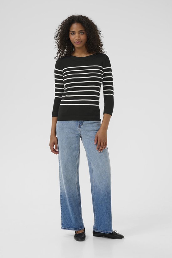 Model met een zwarte trui met horizontale witte strepen en driekwart mouwen, gecombineerd met jeans.