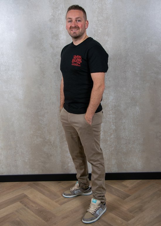 Man met zwarte T-shirt en beige chino, handen in de zakken.
