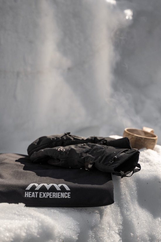 Zwarte wanten op een zwart kussen met het Heat Experience logo, in een besneeuwde omgeving.