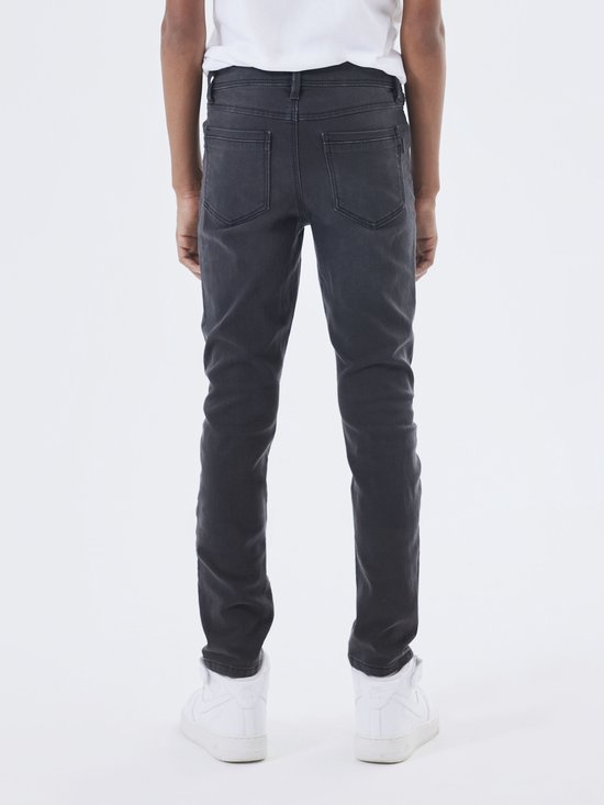 Jongen in grijze slim fit spijkerbroek, staand, gezien vanaf de achterkant.