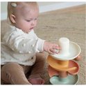 Een baby met een gebreide vest speelt met een spiraaltoren in zachte pasteltinten.