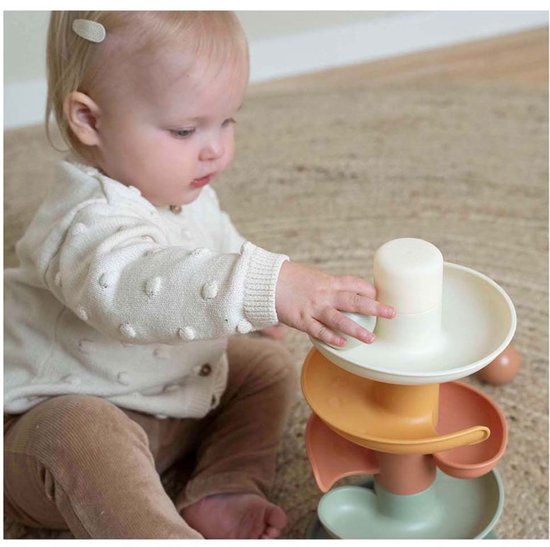 Een baby met een gebreide vest speelt met een spiraaltoren in zachte pasteltinten.
