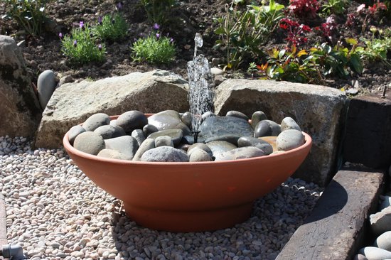 Terracotta fonteinbak gevuld met grijze en bruine stenen, met water dat over de stenen stroomt.