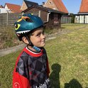 Jongen met groene dinosaurushelm en rood-zwart shirt in de tuin.