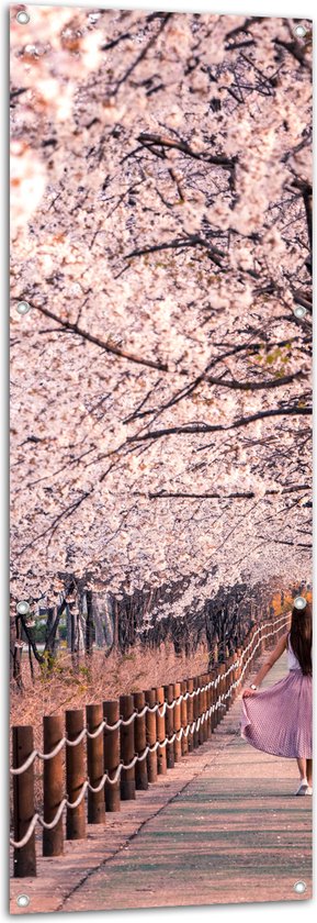 Tuinposter – Voetpad - Persoon - Bomen - Bloesem - Paaltjes - Rok - 50x150 cm Foto op Tuinposter (wanddecoratie voor buiten en binnen)