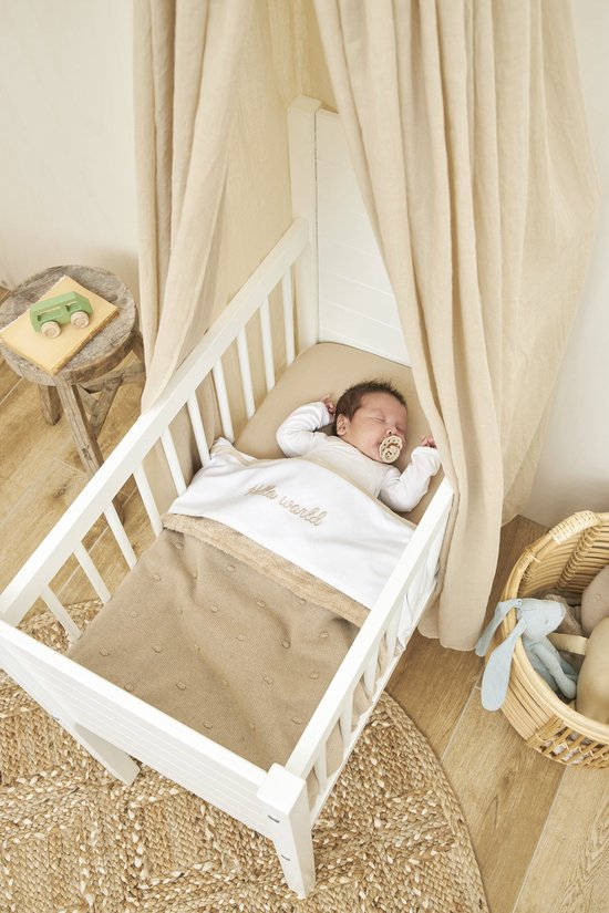 Baby slaapt in een wit wiegje onder een zandkleurige voile. Beddengoed met tekst 'hello world'.