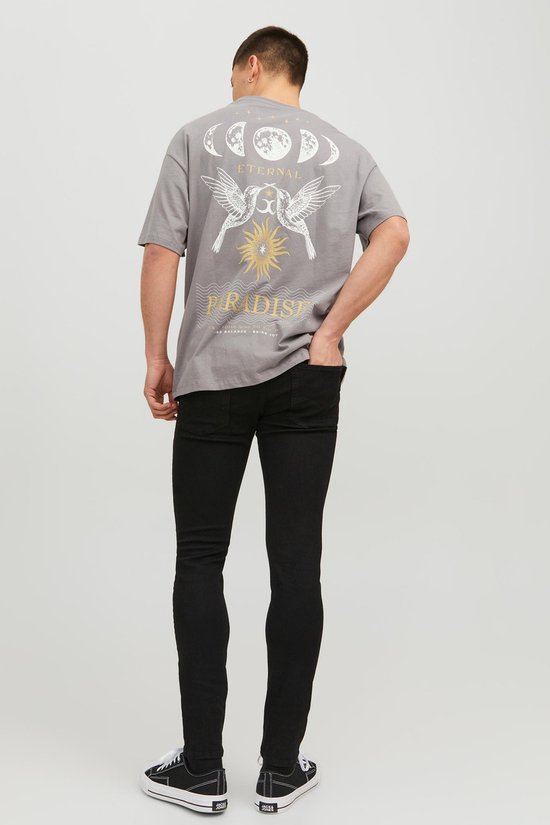 Man met grijze t-shirt met 'Eternal Paradise' print, zwarte skinny jeans en zwart-witte sneakers, van achteren gezien.