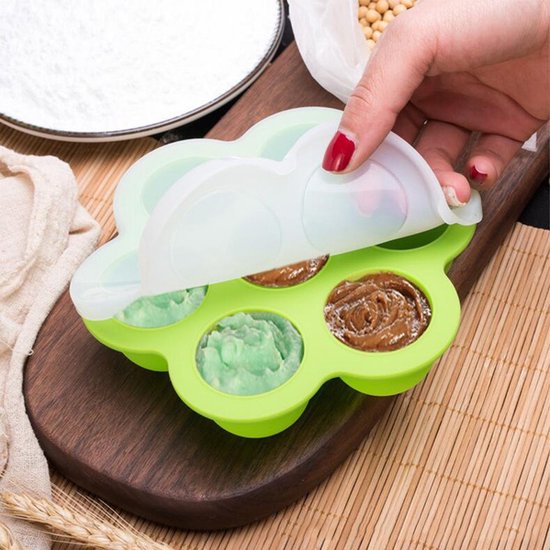 Groen siliconen bakje met babyvoeding, deels bedekt met een wit deksel. Gevuld met groene en bruine puree.