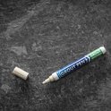 Een witte voegpen met dop ernaast op een donkere, ruwe ondergrond.