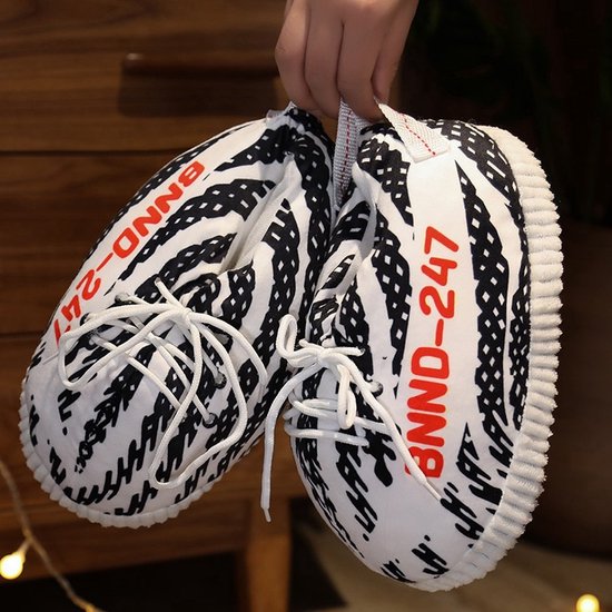 Hand houdt twee zwart-witte sneaker-pantoffels vast met rode BNND-247 tekst.