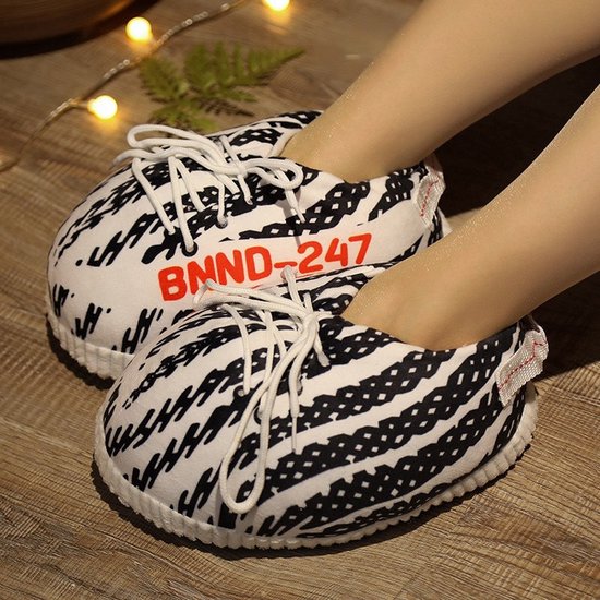Close-up van voeten in zachte zwart-witte sneaker-pantoffels met rode BNND-247 tekst.