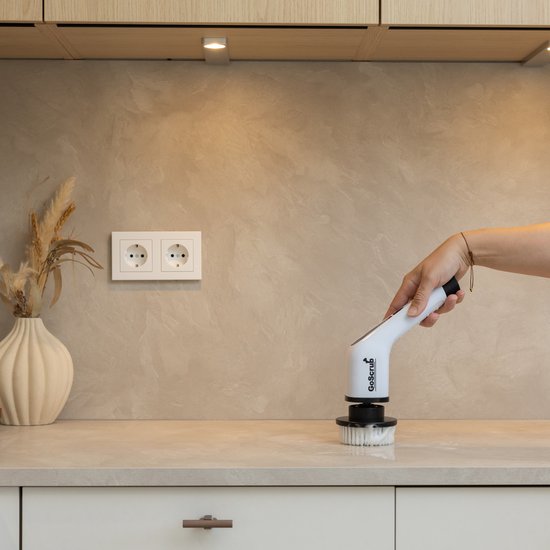 Hand gebruikt de witte elektrische schrobborstel met ronde borstel op een aanrecht.