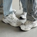 Twee personen dragen witte "DUTCH'D" sneakers met zilveren details en jeans.
