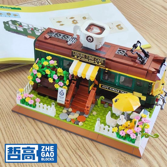 Groene en bruine tram, "Leisure Time Cafe" erop, met koffiekop, bloemen, witte hekjes en een parasol.
