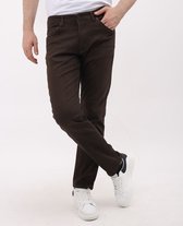 Man met bruine jeans met vijf zakken en witte sneakers, staand met gekruiste benen.