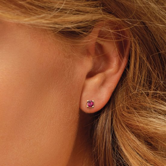 Clou d'oreille en or avec pierre rouge porté à l'oreille par une femme.