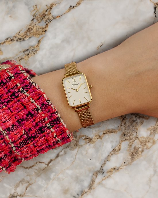 Gouden rechthoekig horloge met mesh band om de pols, gedragen met een roze-rode jas.
