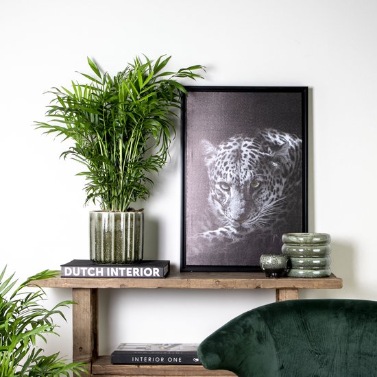 Gezonde groene kamerplant met lange, smalle bladeren in een gegroefde groene pot op een houten plank, naast een schilderij van een luipaard.