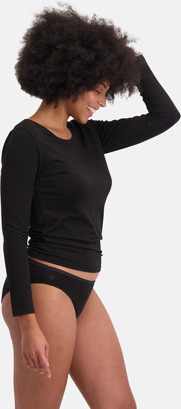 Vrouw met afro-kapsel in zwart longsleeve shirt en zwarte slip, staand op witte achtergrond.