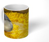 Mok - Een grote lepel schept de gele risotto uit een pan - 350 ML - Beker