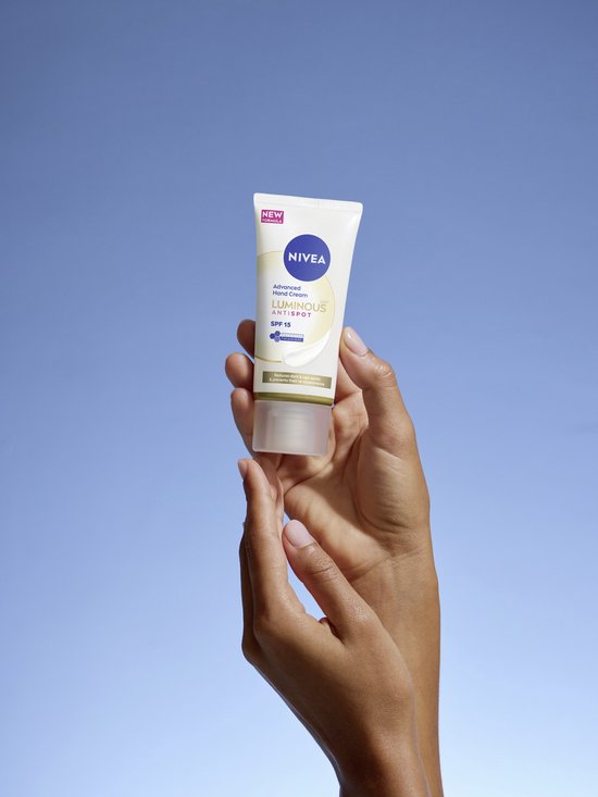 Handen houden een NIVEA Luminous 630 Anti-Spot geavanceerde handcrème met SPF 15 vast tegen een blauwe hemel.