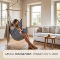 Een vrouw met baby in een blauwgrijze hangstoel in een woonkamer.