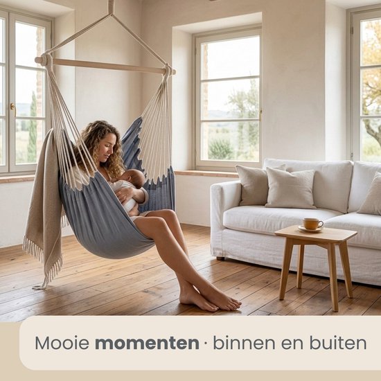 Een vrouw met baby in een blauwgrijze hangstoel in een woonkamer.
