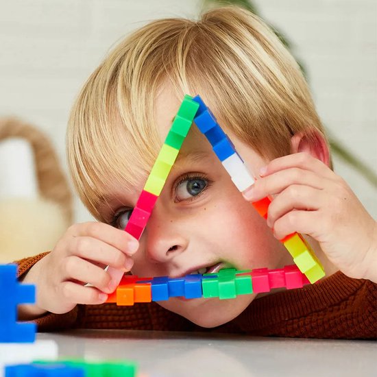 Jongetje met blond haar houdt een driehoek vast gemaakt van veelkleurige Plus-Plus bouwstenen.