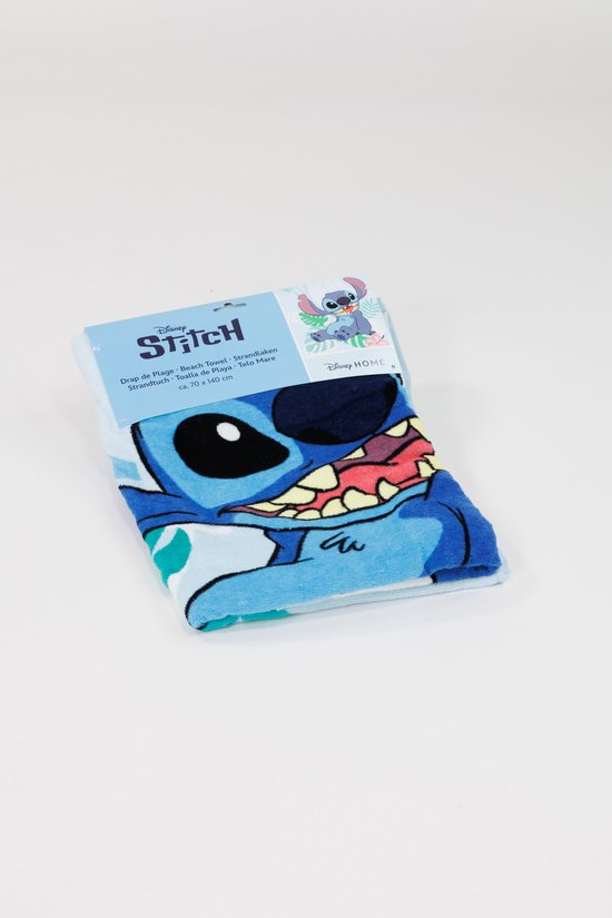 Een gevouwen lichtblauwe strandlaken met Stitch erop, met een verpakking met Stitch en tekst 'Disney Stitch Strandlaken'.