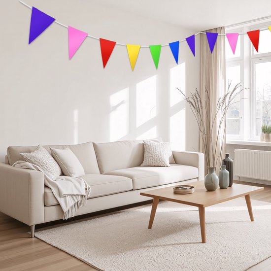 Guirlande festive avec des fanions triangulaires multicolores au-dessus d'un canapé beige dans un salon.