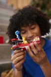 Kind met krullend haar houdt het gebouwde rode LEGO Tornado-vliegtuig met Sonic en Tails minifiguren vast.