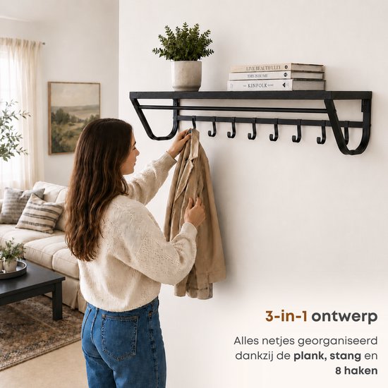 Vrouw hangt jas aan zwarte wandkapstok met plank, stang en 8 haken.