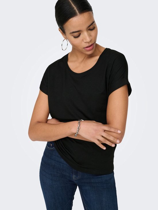 Model van dichtbij in een zwart T-shirt met opgerolde korte mouwen en een jeans.