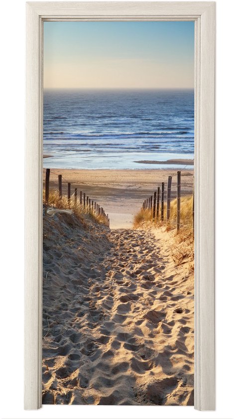 Zandpad met duinen en hekjes naar de zee, strand en heldere lucht.