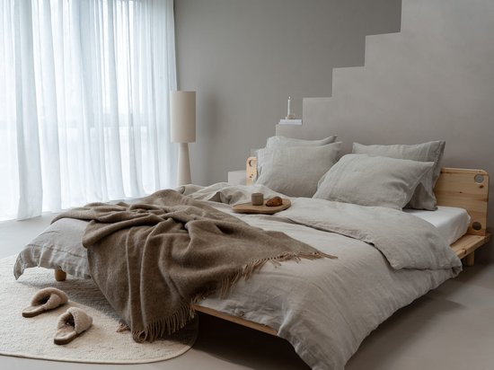 Luxe slaapkamer met een bed met beige linnen beddengoed, een bruine plaid, pantoffels en een dienblad met croissants.