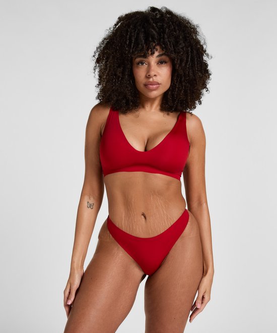 Model draagt rode beha met diepe V-hals en bijpassende slip.