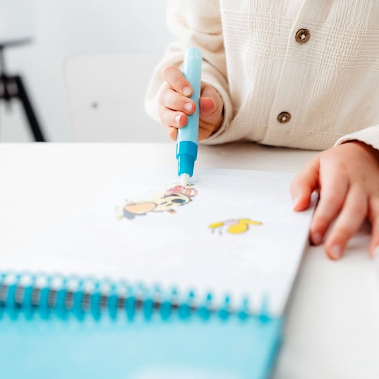 Close-up van een kinderhand die met een blauwe pen in een schetsboek met illustraties tekent.