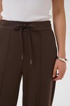 Detailopname van een bruine broek met strikceintuur, flatteuze naden en een zilveren armband.