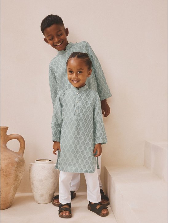 Twee jongens dragen een lichtgroene kurta met bladmotief en een witte broek, staand in een beige studio.