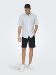 Man draagt een lichtblauwe Only & Sons korte mouwen overhem met zwarte shorts.