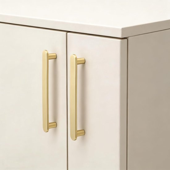 Twee matte messing handgrepen met gouden kleur op crème kasten.