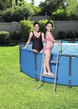 Vrouw en meisje in badkleding bij ronde blauwe zwembad met grijze ladder.