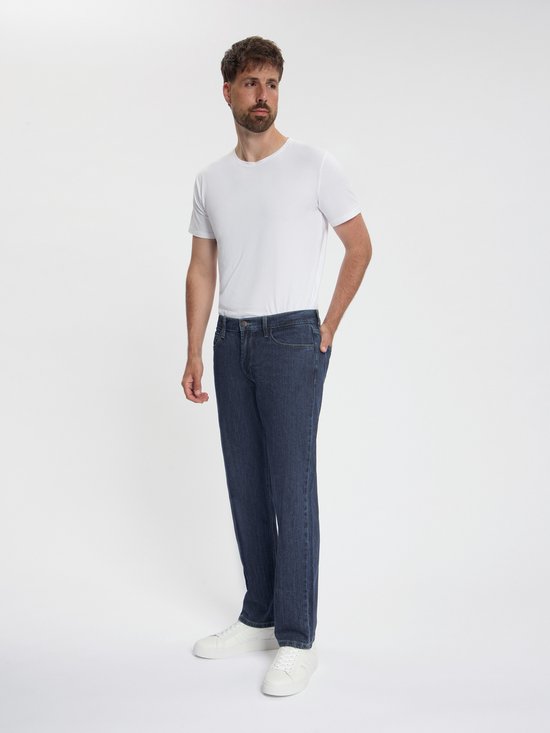 Man in donkerblauwe MASKOVICK jeans met gele stiksels en witte sneakers.