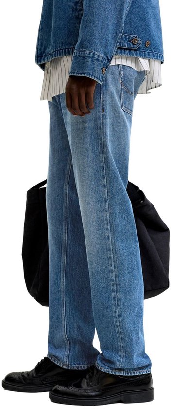 Zij-aanzicht van de benen van een man in een blauwe spijkerbroek met rechte pasvorm en zwarte schoenen.