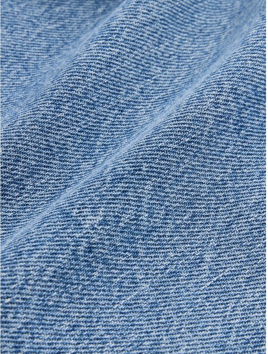 Gedetailleerde close-up van blauw denim met een zichtbare textuur en lichte kreuken.