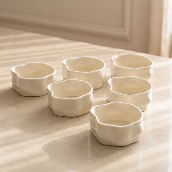 Zes beige keramieken snackbakjes met onregelmatige vormen, op een tafel.