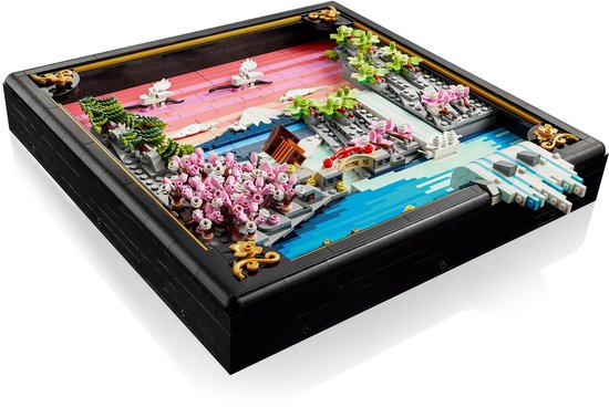 Een LEGO-weergave van een Japans landschap met kersenbloesems, rivier, brug en bergen in een zwarte lijst.